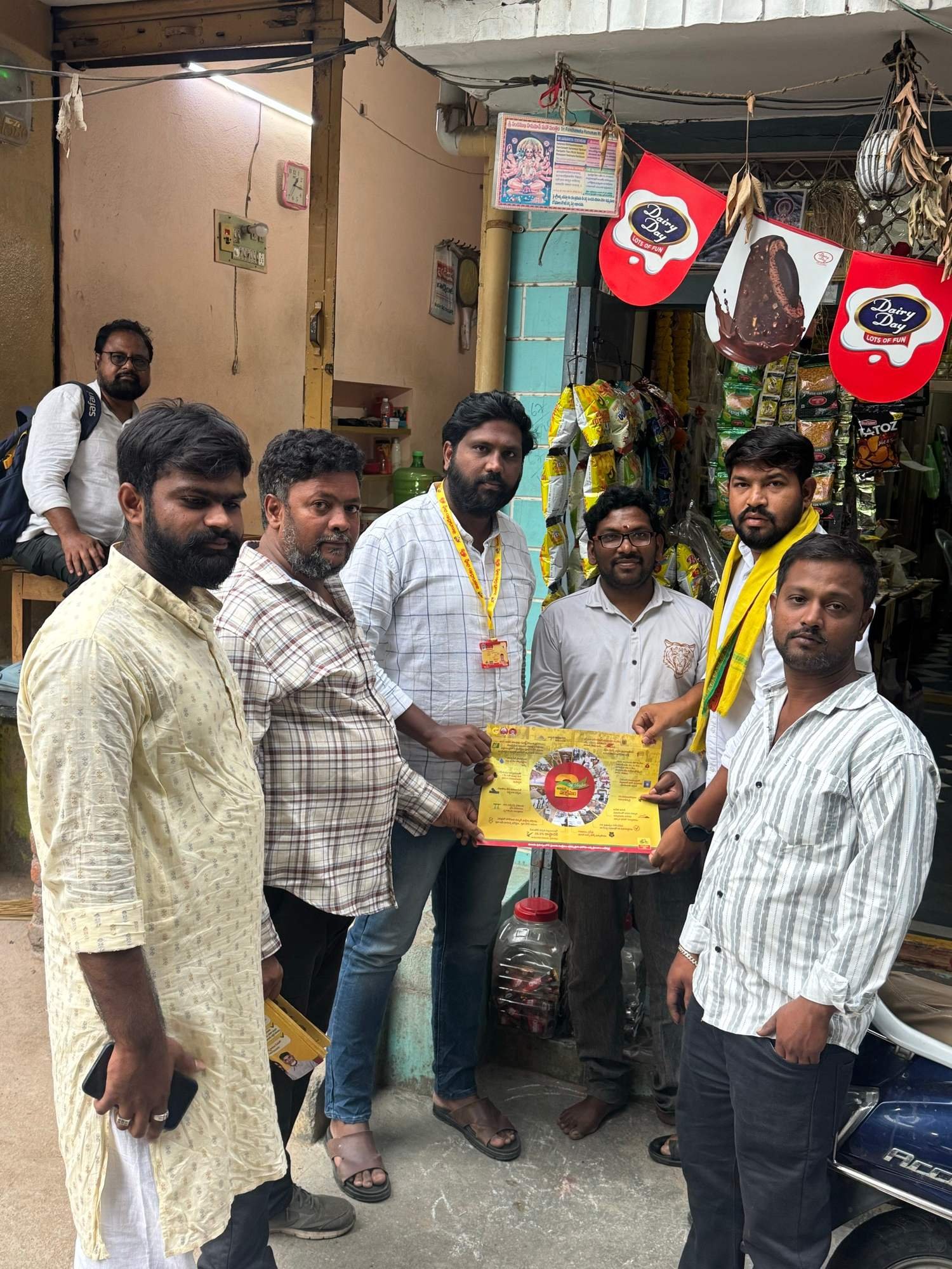 స్థానిక దుకాణం వద్ద ప్రచార పోస్టర్ పట్టుకున్న పార్టీ కార్యకర్తలు
