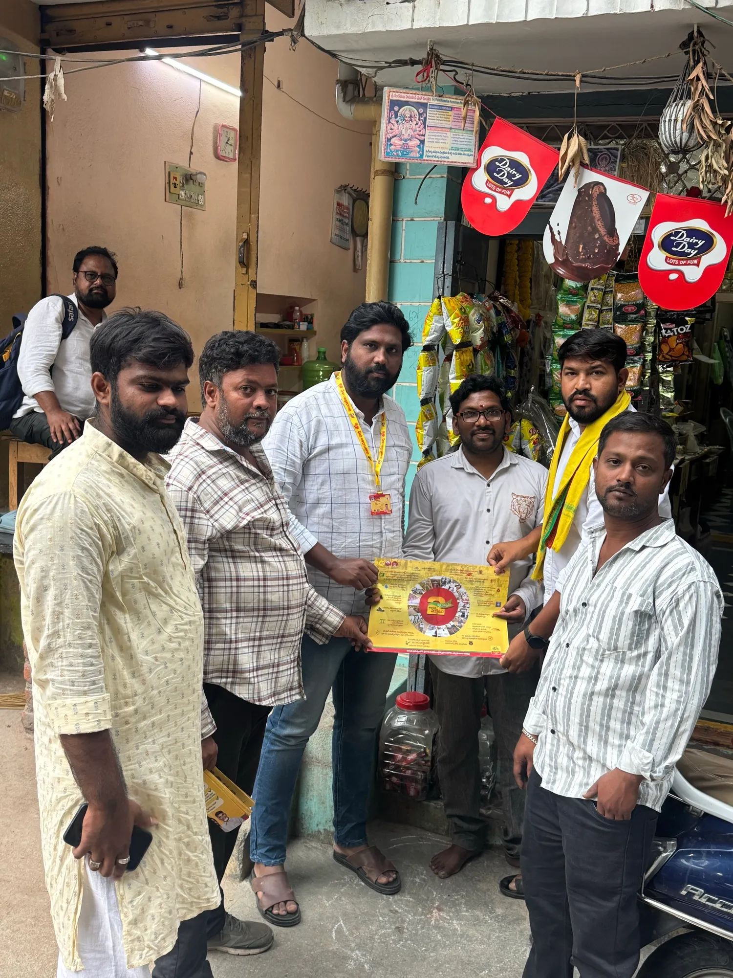 స్థానిక దుకాణం వద్ద ప్రచార పోస్టర్ పట్టుకున్న పార్టీ కార్యకర్తలు